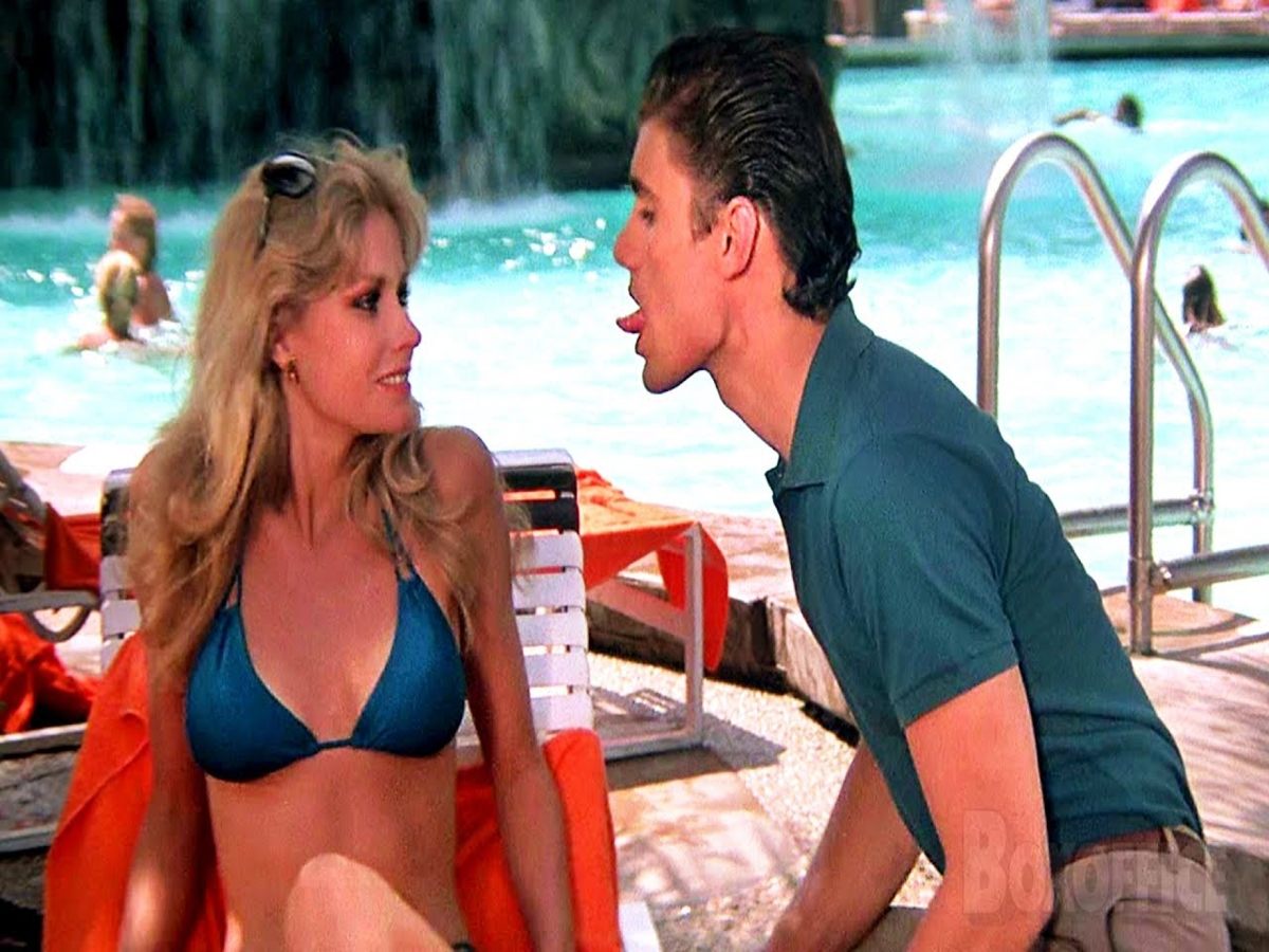 Michelle Pfeiffer as Elvira in Scarface, wearing a luxurious gold satin two-piece with flared trousers and a flowing slip top.