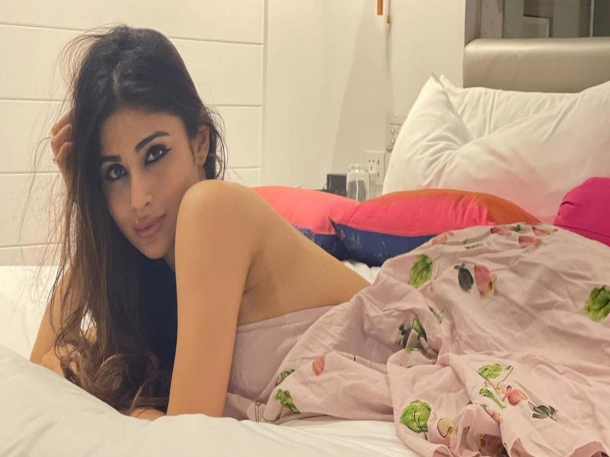 Mouni Roy sitting on a bed wearing a white bathrobe