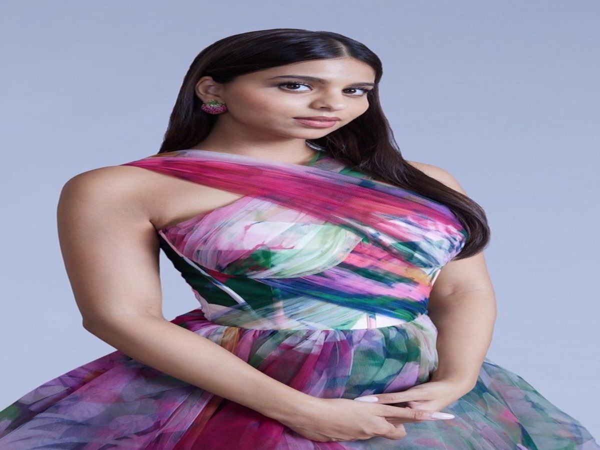 A person wearing a colorful dress with an asymmetrical neckline and a flowing skirt, showcasing a beautiful blend of pink, green, and blue hues.