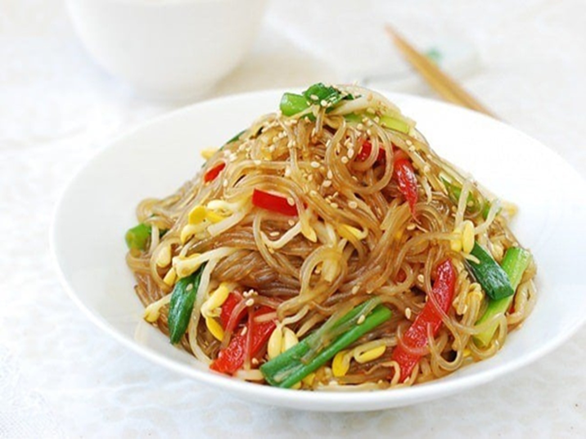 A bowl of shiny Korean noodles cooked in soybean sprout broth, topped with scallions and sesame seeds