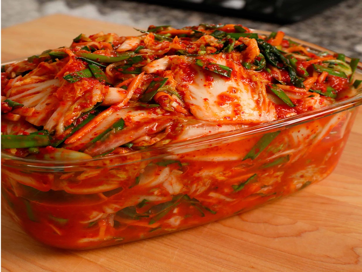 Hands coating napa cabbage leaves with vibrant red vegan kimchi paste