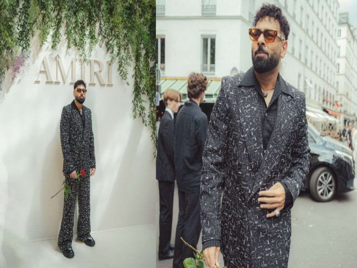 Badshah in black loafers and an Amiri tote with floral design, accessorized with a diamond 'Om' pendant and a luxury watch.