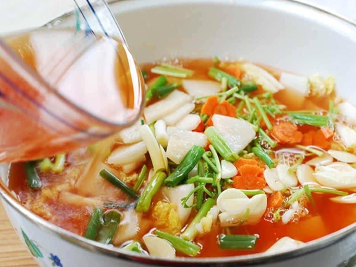 Glass bowl filled with pink‑hued nabak kimchi broth and neatly squared pieces of radish and napa cabbage