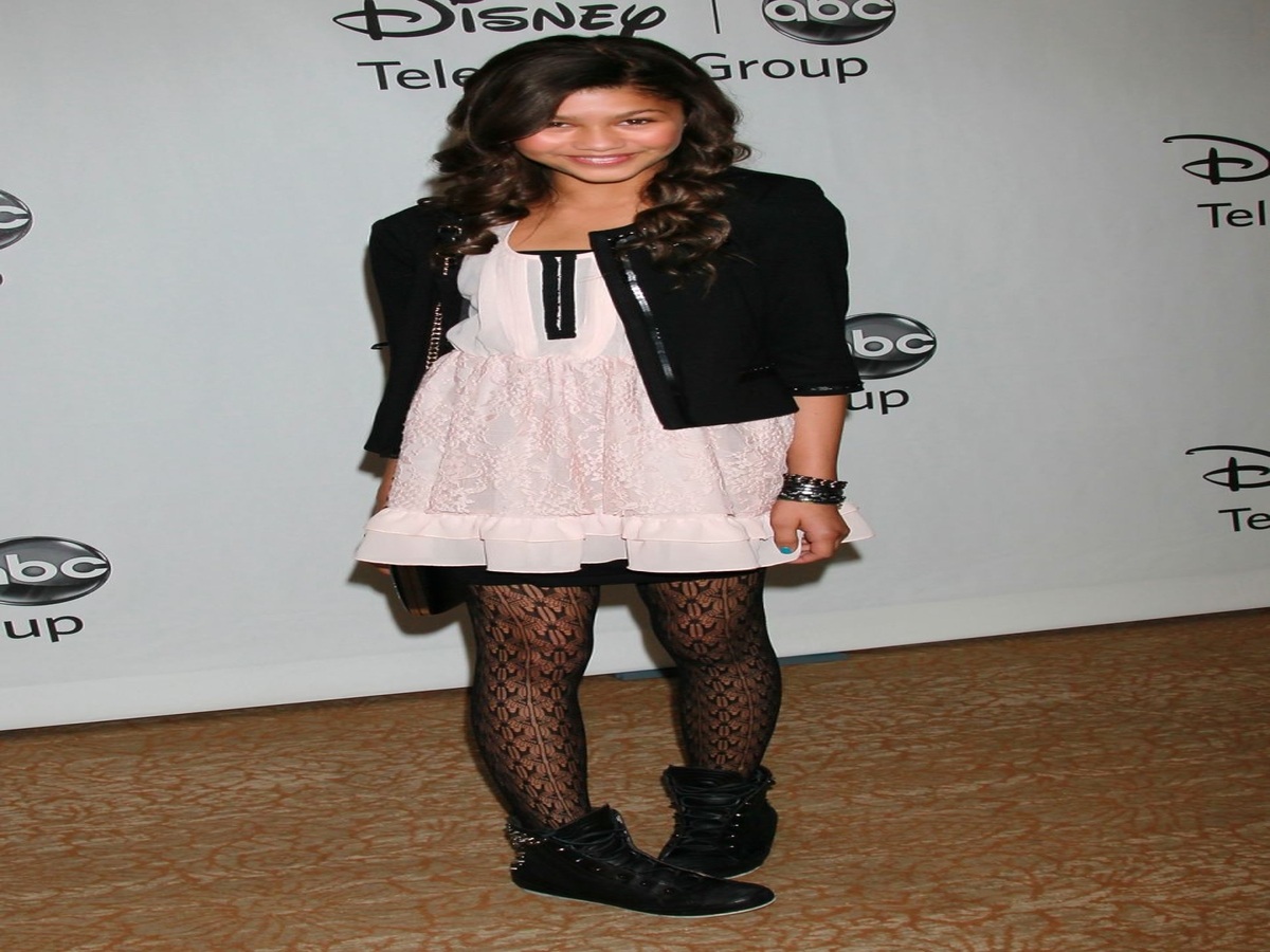 Zendaya at a 2010 Disney event, displaying her youthful fashion sense with a minidress, black jacket, patterned tights, and hi-top sneakers.
