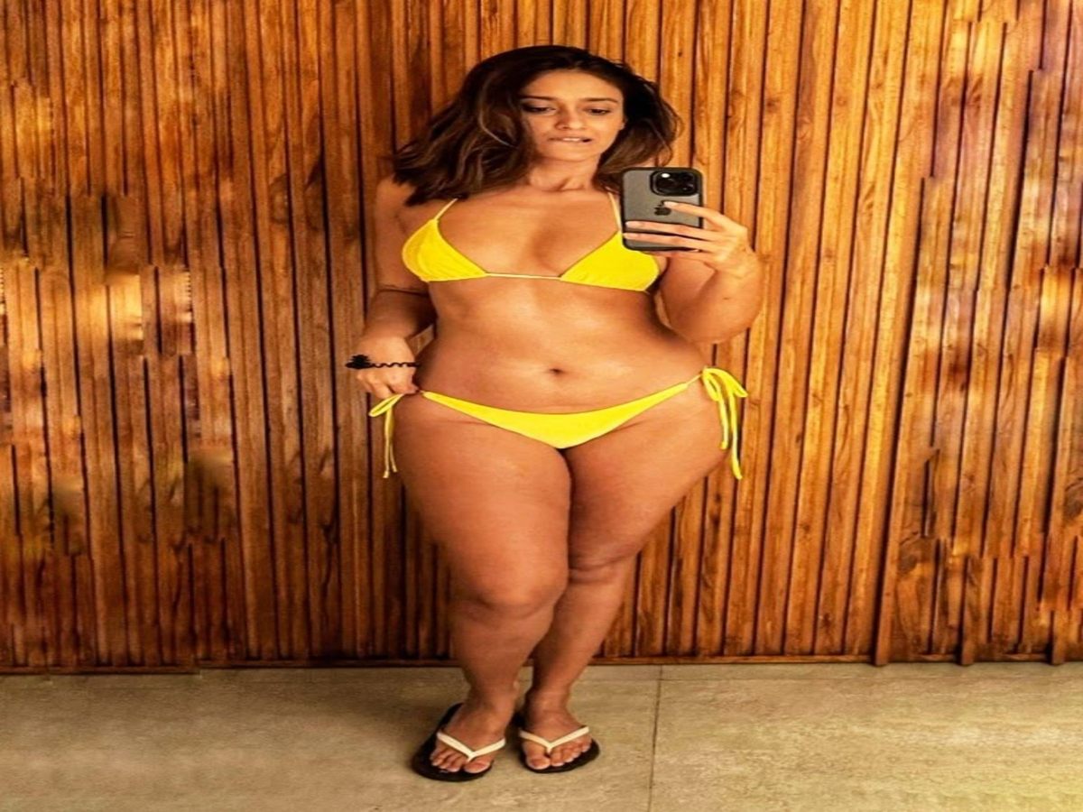 Woman in a bright yellow bikini, posing confidently in front of a wooden background.