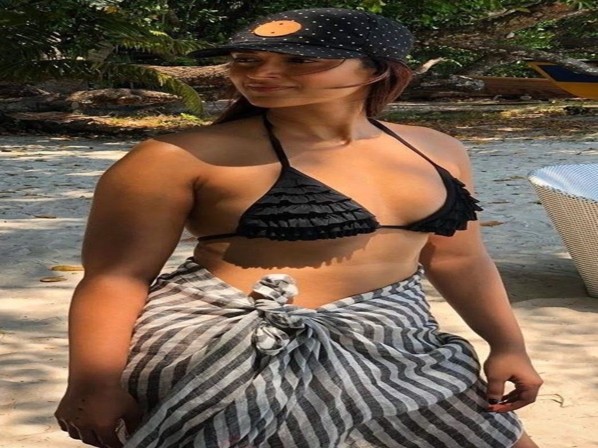 Woman in a chic black bikini and striped wrap, posing on the beach.