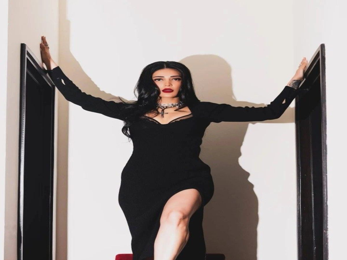 A fashionable individual showcasing a chic black dress, exuding confidence and sophistication in a striking pose.