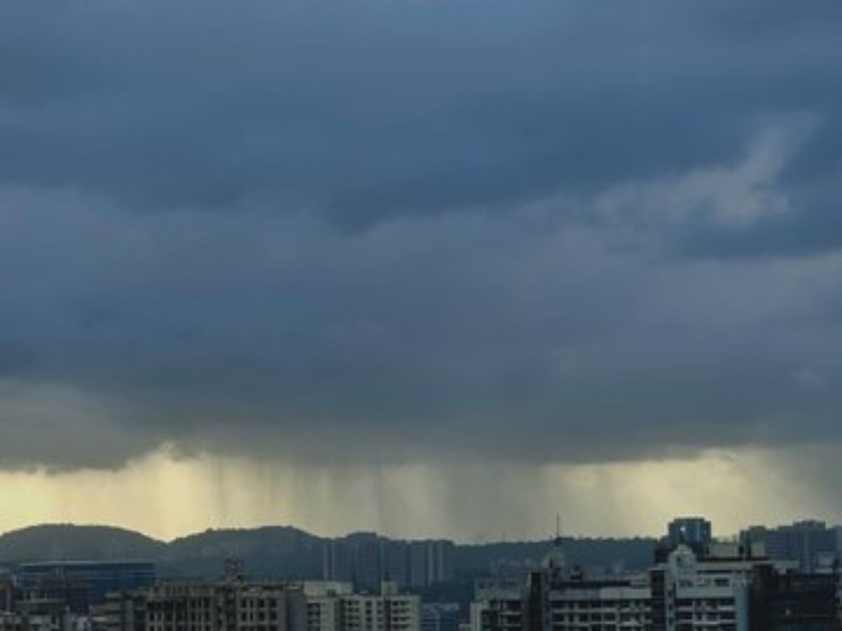 Dark monsoon clouds and rain showers are seen over town homes and distant hills at some point of sunset.