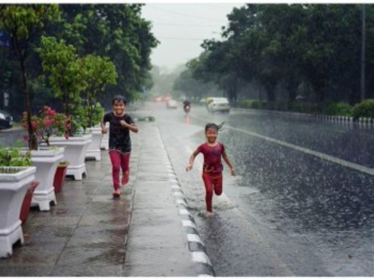 Two happy children running barefoot in the rain on a city street during the monsoon season.