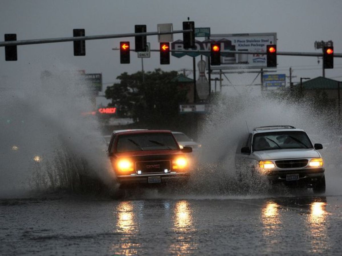 A car splashing through water on a rainy street, blurry due to speed.