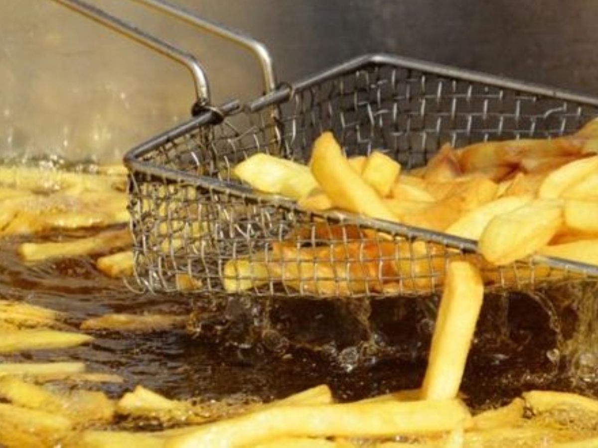 Close-up of French fries being deep-fried in hot oil, rising out of a fryer basket.