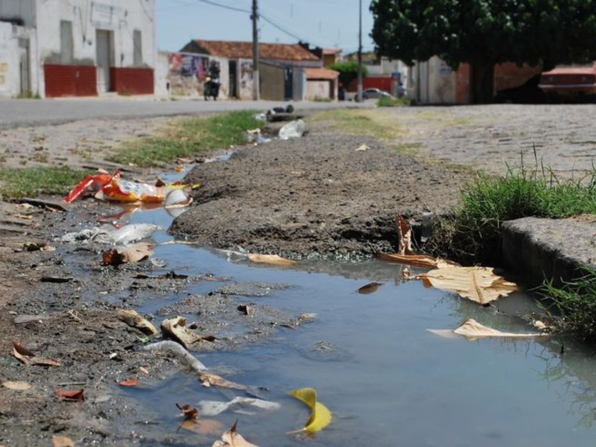 Stagnant dirty water and trash collected along the roadside near a drain during monsoon.