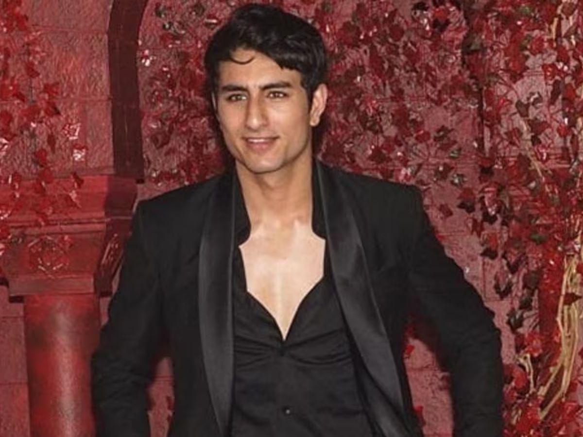 Ibrahim Ali Khan smiling in a black suit with a red floral background