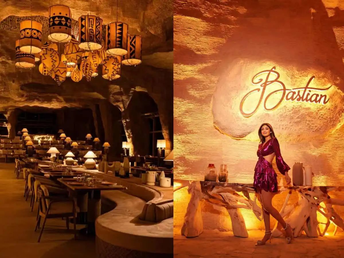 Warm-lit rustic wall with ‘Bastian’ logo carved and glowing, surrounded by cozy seating and artistic décor in an upscale dining setup.