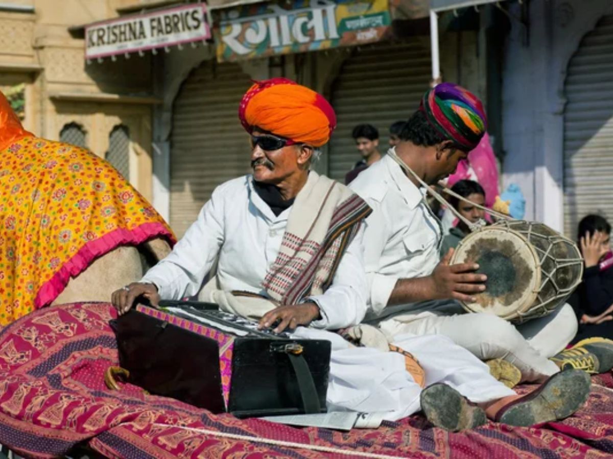 Elderly musician playing harmonium and singing in a public corner.