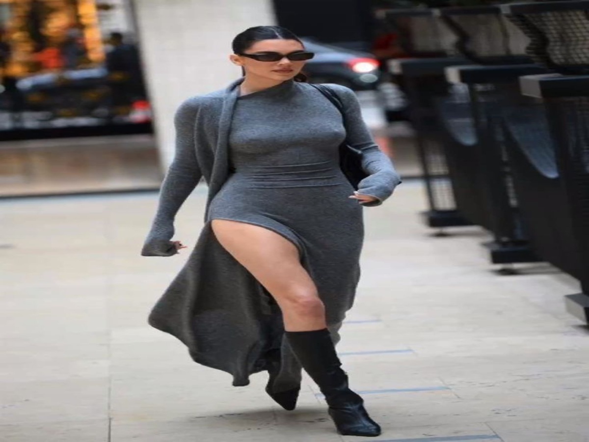 A model walking confidently in a grey knit dress with a high slit, complemented by a long cardigan and knee-high boots.