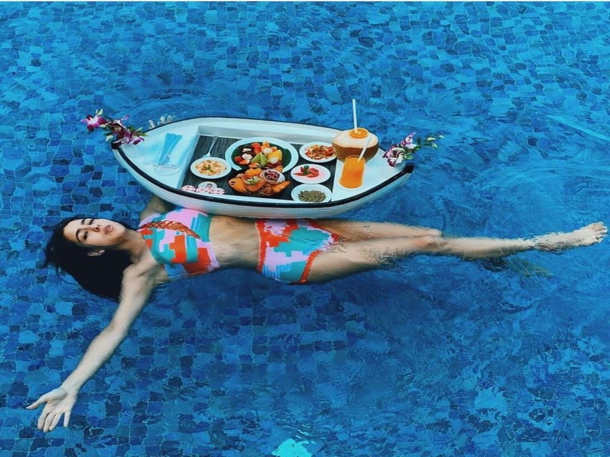 A model lounging in a vibrant bikini, floating in a pool with a tray of delicious food and drinks, enjoying a luxurious summer day.