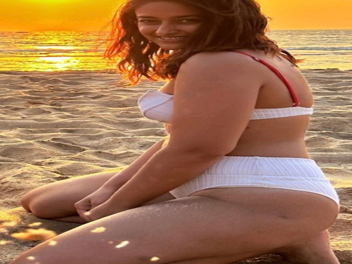 Woman kneeling on the beach at sunset, wearing a stylish two-piece swimsuit.