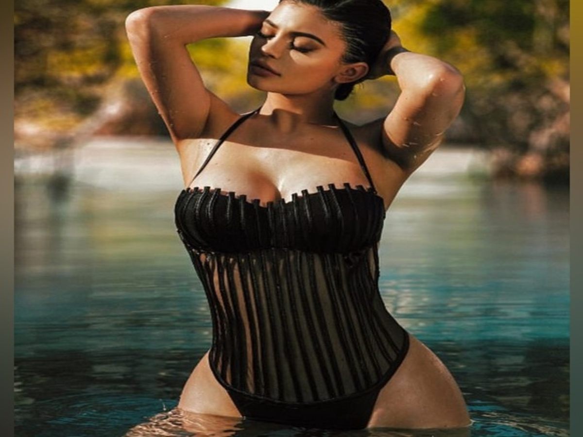 A stylish individual wearing a striking black swimsuit with vertical stripes, posing gracefully in water.