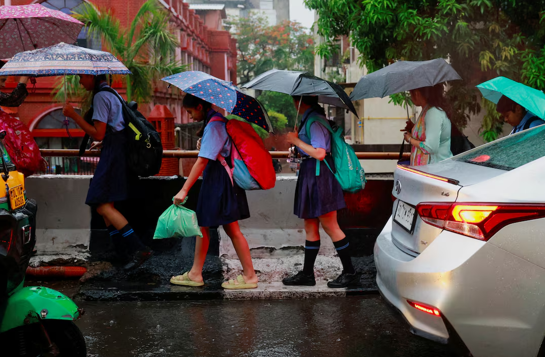 Children using umbrellas in rain near school in Delhi