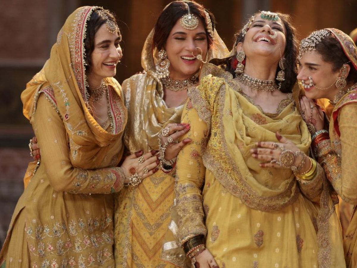 Group of Heeramandi women in coordinated golden ghararas with embroidered dupattas.