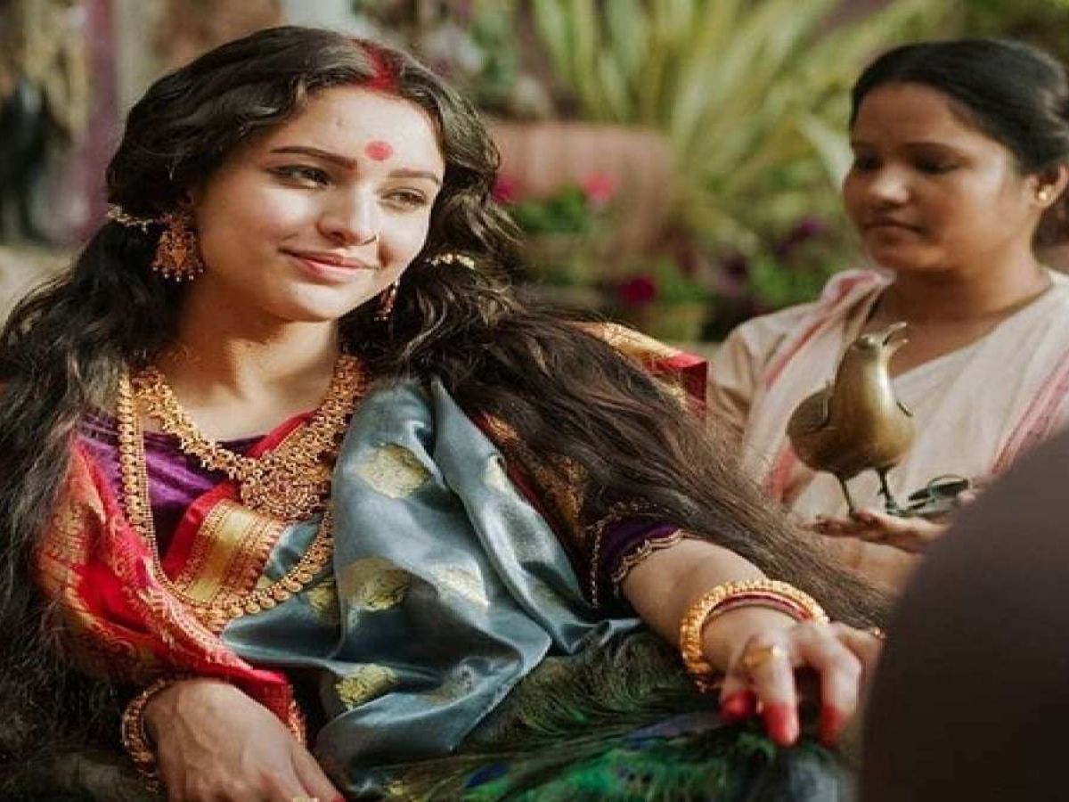 Tripti Dimri dressed in traditional Bengali attire, smiling softly with intricate gold jewellery and sindoor, seated gracefully with a maid behind her