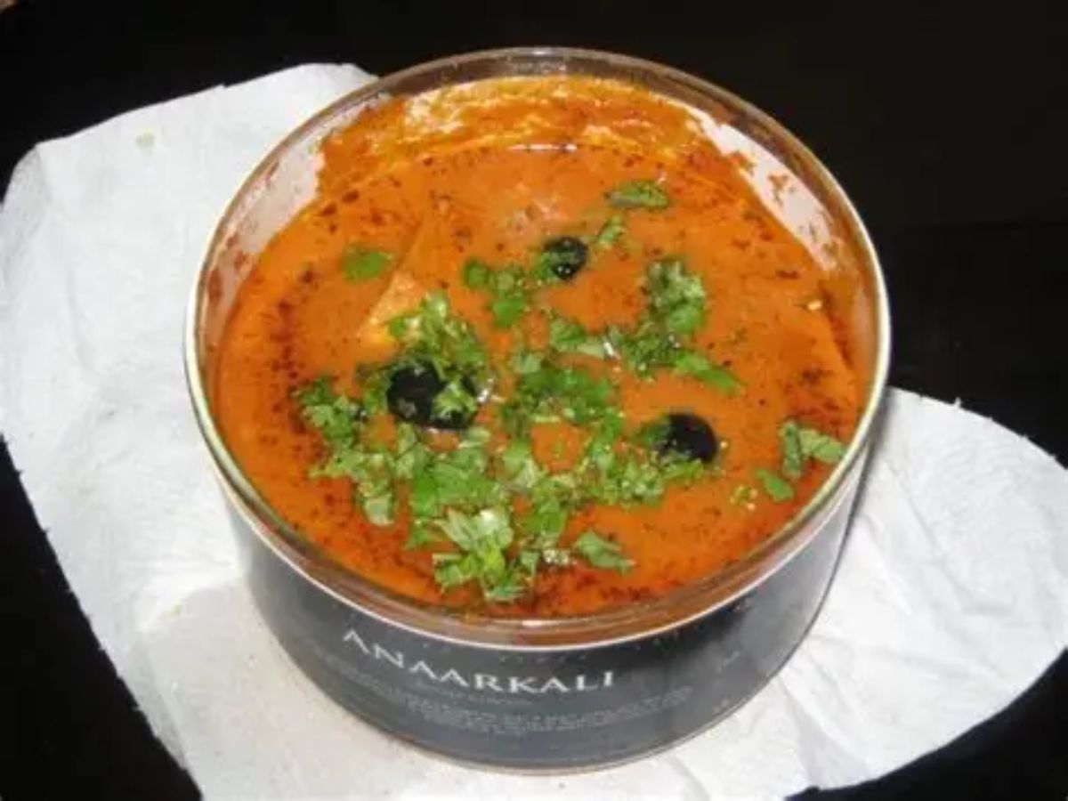 Rich butter chicken served in a black round container, garnished with coriander and olives